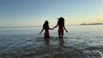Two naked beauties swim in the sea at dawn